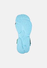 Ljusblå gummisula med texturerade mönster och spår; har gröna remmar och varumärkesprägling på ytan.