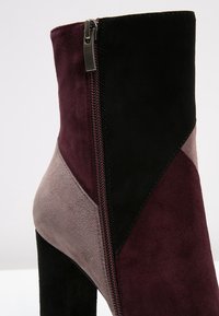 Kotníkové boty s kombinací černé, burgundské a šedé semišové kůže, bočním zipem a silným podpatkem. Geometrický panelový design zvýrazňuje barevný kontrast.
