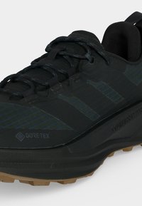 Μαύρο αδιάβροχο αθλητικό παπούτσι Gore-Tex με υφή στην σόλα, στρογγυλεμένη μύτη και κορδόνια, σχεδιασμένο για υπαίθριο τρέξιμο ή πεζοπορία.