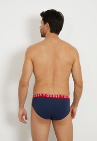 Herrenunterwäsche in marineblau mit einem roten und weißen "GUESS" Logo-Bund, glatte Textur und einer eng anliegenden Passform.
