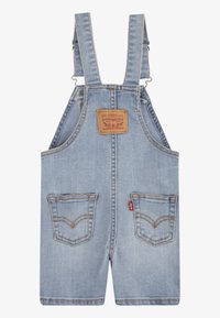Ljusblå denimoverall med justerbara remmar, ett varumärkesmärke och två framfickor med förstärkt sömnad och en klassisk design.