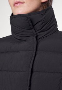 Svart puffjacka med hög krage, kviltad struktur och en slät finish. Tyget verkar vara lätt och vattentåligt.