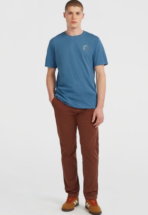 Blauwe katoenen t-shirt met korte mouwen, ronde halslijn en een logo-print. Gecombineerd met een paar bruine rechte broek en bruine sneakers.