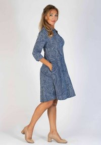 Niebieska sukienka w wzór paisley z rękawami o długości trzech kwart, okrągłym dekoltem i bocznymi kieszeniami, zestawiona z beżowymi butami na słupku.