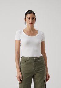 Hvit ribbet kortermet bodysuit med scoop-hals, kombinert med olivengrønne cargo-bukser med sidelommer og knappeåpning.