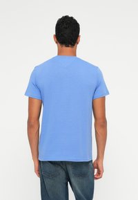 Majica s kratkimi rokavi, okroglim ovratnikom v svetlo modri barvi iz bombaža. Ima gladko teksturo, preprost dizajn in sproščen kroj.