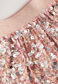 Pink fabric with sequins in circular shapes, featuring a textured, shiny surface. A wide, elastic waistband in a matching color completes the design.