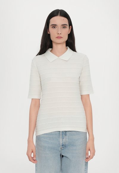 Lysfarvet, kortærmet strik polo skjorte med et tekstureret stribet mønster og bølgede kanter. Båret med blå denim jeans.