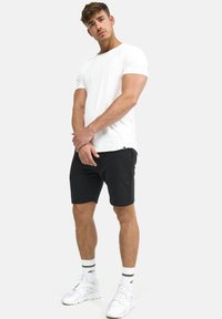 White short-sleeve t-shirt, relaxed fit; black athletic shorts with side pockets; white sneakers with contrasting accents; casual style.