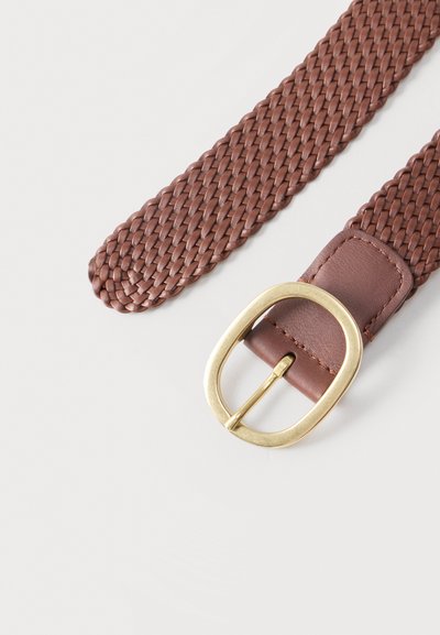 Καφέ υφαντή δερμάτινη ζώνη με στρογγυλεμένη μπρούτζινη αγκράφα σε απλή ανοιχτή επιφάνεια, που δείχνει λεπτομερή υφή και ραφές.