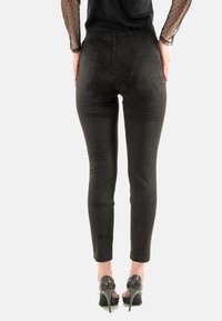Pantalones negros ajustados con una textura suave similar al ante. Longitud hasta los tobillos con una cintura alta, combinados con zapatos de tacón alto y brillantes.