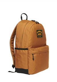 Sac à dos en tissu brun avec des accents noirs, une poche avant et un patch logo. Il possède des bretelles rembourrées et une fermeture à glissière.