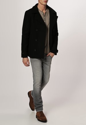 Schwarzer Peacoat mit doppeltknöpfigem Verschluss, getragen über einem grauen Henley, kombiniert mit hellgrauen Jeans und braunen Wildlederschuhen.