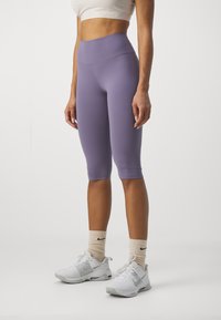 Lila knälånga leggings gjorda av elastiskt tyg, med en hög midja och slät yta, i kombination med vita sneakers och lätta strumpor.