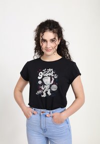 Černé bavlněné tričko s ohrnutými rukávy, zdobené grafikou postavy mezi planetami a hvězdami. Modelka má na sobě světle modré džíny.
