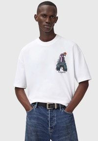 Hvid bomulds T-shirt med et grafisk motiv af en løftet næve med en pink rose. Rund halsudskæring, korte ærmer, parret med blå denim jeans og et sort bælte.