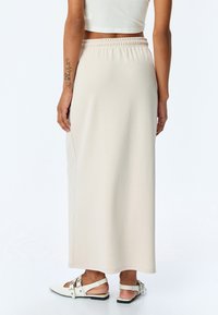 Jupe beige longueur cheville en matériau doux et extensible avec une taille élastique, présentant une texture lisse et des détails de couture latérale.