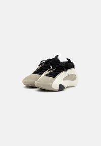 Sportowe sneakersy w odcieniach beżu, czerni i bieli. Smukła konstrukcja z teksturowanej tkaniny i gumowymi akcentami. Posiadają sznurówki i zaokrąglony kształt noska.