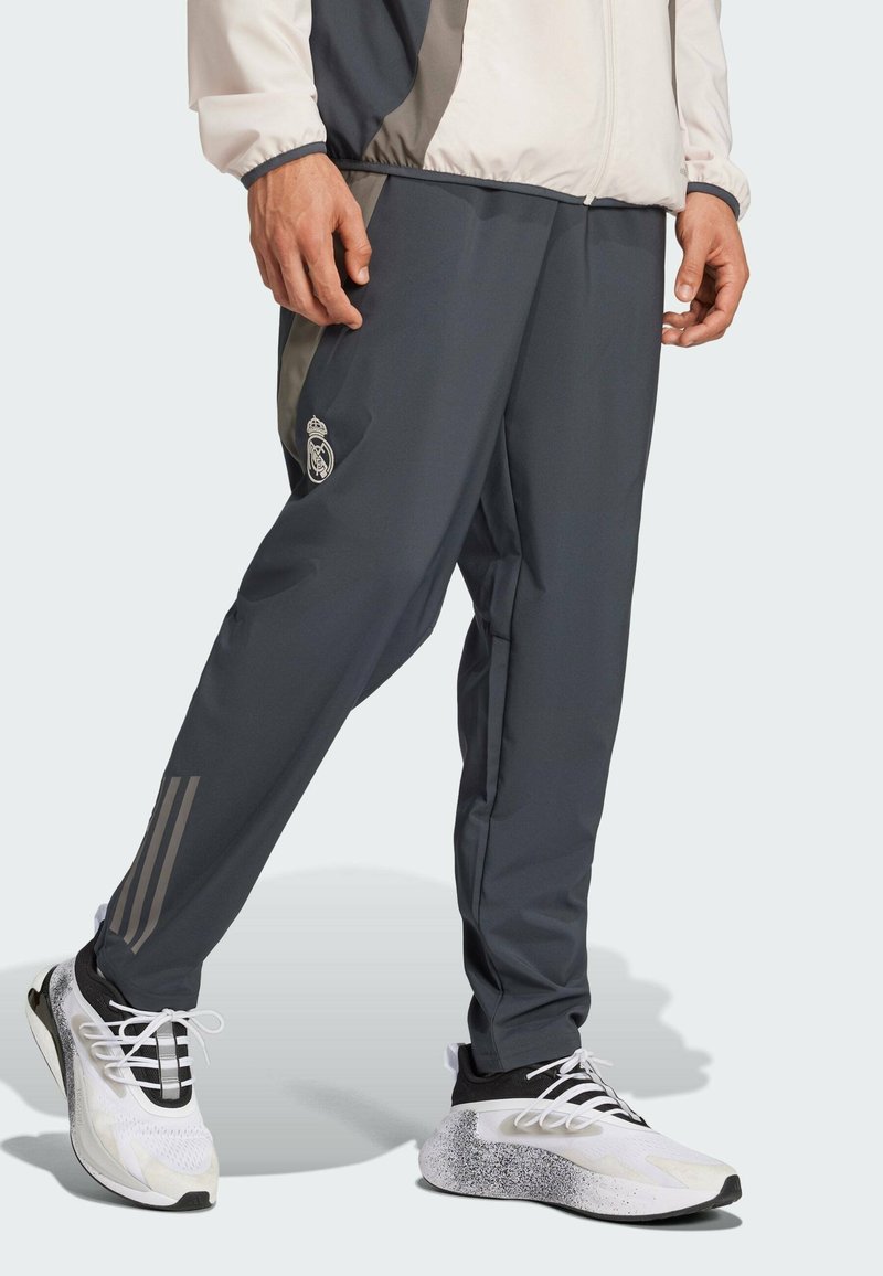 Grijze sportbroek met een slim fit, voorzien van een lichtgrijze accent en logo op de dij. Gecombineerd met witte sneakers met zwarte en gespikkelde details.