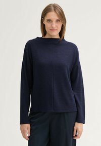 Pull en maille bleu marine, à coupe large, avec des manches longues et un col haut. Tissu texturé et ourlet droit. Design simple sans motifs.