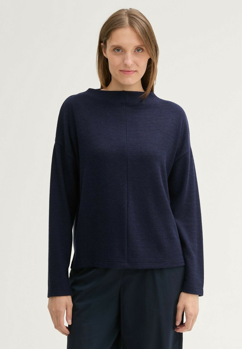 Pull en maille bleu marine, à coupe large, avec des manches longues et un col haut. Tissu texturé et ourlet droit. Design simple sans motifs.
