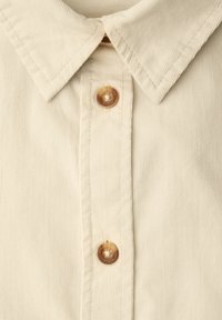 Chemise en velours côtelé beige avec un col pointu et deux boutons marron sur la patte de boutonnage centrale avant.