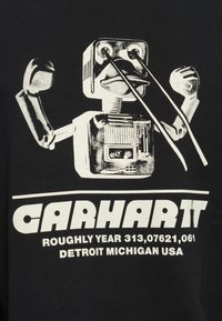 Zwarte T-shirt met een witte afbeelding van een robot met omhoog gestoken armen, met de tekst "Carhartt" en extra tekst eronder, gedrukt op een gladde stof.