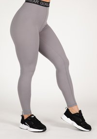 Pilkos leggingai, pagaminti iš tampraus audinio, su juodu liemeniu, kuriame yra "GORILLAWEAR" logotipas. Prisiderinę su juodais sportiniais batais.