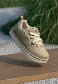 Beige joggesko med strukturert overdel, rund tå og snøredesign. Har polstret krave og tykk, nøytral farget såle.