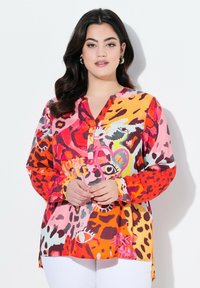 Chemise à boutons multicolore avec des motifs léopard et abstraits en rose, orange et rouge, offrant une coupe ample et des manches longues.