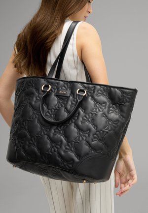 Sac fourre-tout noir matelassé en cuir texturé, avec quincaillerie dorée, deux poignées, et une étiquette logo sur le devant.