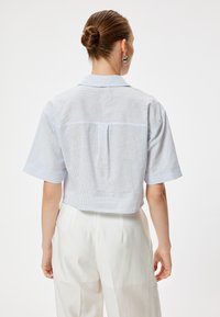 Camisa corta de manga corta en azul claro con rayas blancas, con un panel de yugo en la parte posterior y un cuello clásico, hecha de un tejido ligero.
