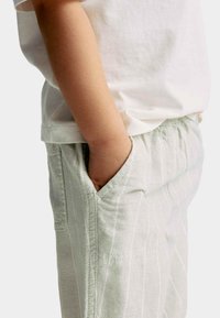 Lichtgrijze gestreepte broek met een elastische tailleband en zijzakken, gedragen met een wit katoenen T-shirt, wat een ontspannen pasvorm laat zien.