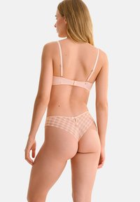 Ensemble de lingerie rose clair comprenant un soutien-gorge lisse avec des bretelles ajustables et un string à dos en dentelle assorti, décoré d'un motif à carreaux et d'un détail en nœud.
