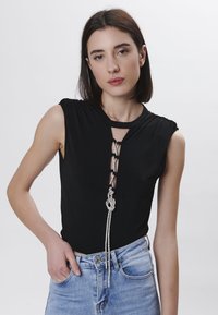 Top negro sin mangas con un diseño de encaje frontal y un acento de cuerda plateada, combinado con jeans de cintura alta en un tono azul claro. Textura suave.
