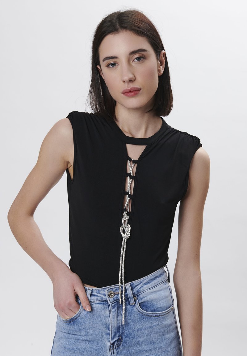 Top negro sin mangas con un diseño de encaje frontal y un acento de cuerda plateada, combinado con jeans de cintura alta en un tono azul claro. Textura suave.