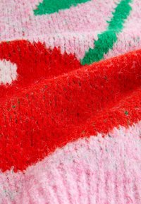 Pletená látka s výraznými vzormi v červenej, ružovej a zelenej farbe, s textúrovaným, chlpatým povrchom a viditeľnými vláknami po celej ploche.