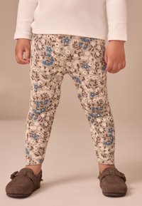 Kwiatowe legginsy w kremowym kolorze, z niebieskimi i brązowymi kwiatami oraz prążkowaną fakturą. Do tego brązowe zamszowe buty wsuwane.