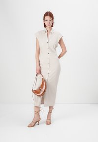 Robe beige à boutons avec manches courtes, dotée d'une fente et de boutons argentés. Associée à un sac à épaule en croco marron et des talons à lanières.