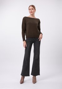 Dunkelgrüner gestrickter Pullover mit weitem Ausschnitt, kombiniert mit schwarzen Schlagjeans und beigen, schulterlangen Stiefeletten mit Absatz. Glatte Textur insgesamt.