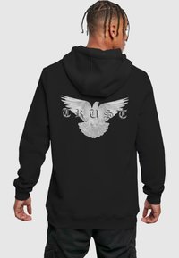 Haut à capuche noir présentant un grand graphisme en blanc d'une colombe en plein envol, avec le mot "CONFIANCE" en lettres argentées en dessous. Tissu doux avec une coupe décontractée.