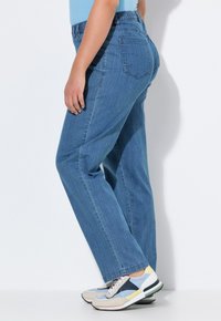 Vaqueros de mezclilla azul claro con un corte relajado, que presentan una pierna recta y bolsillos laterales. Combinados con zapatillas deportivas de colores múltiples.