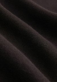 Crni pamuk s glatkom teksturom, s finim rebrastim uzorkom i suptilnim sjajem, uređen u mekim, prozračnim naborima.