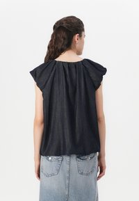 Mørk denim topp med fladdrende ermer, samlet halslinning og løs passform. Brukt med en lyseblå denimskjørt med lommepatches.