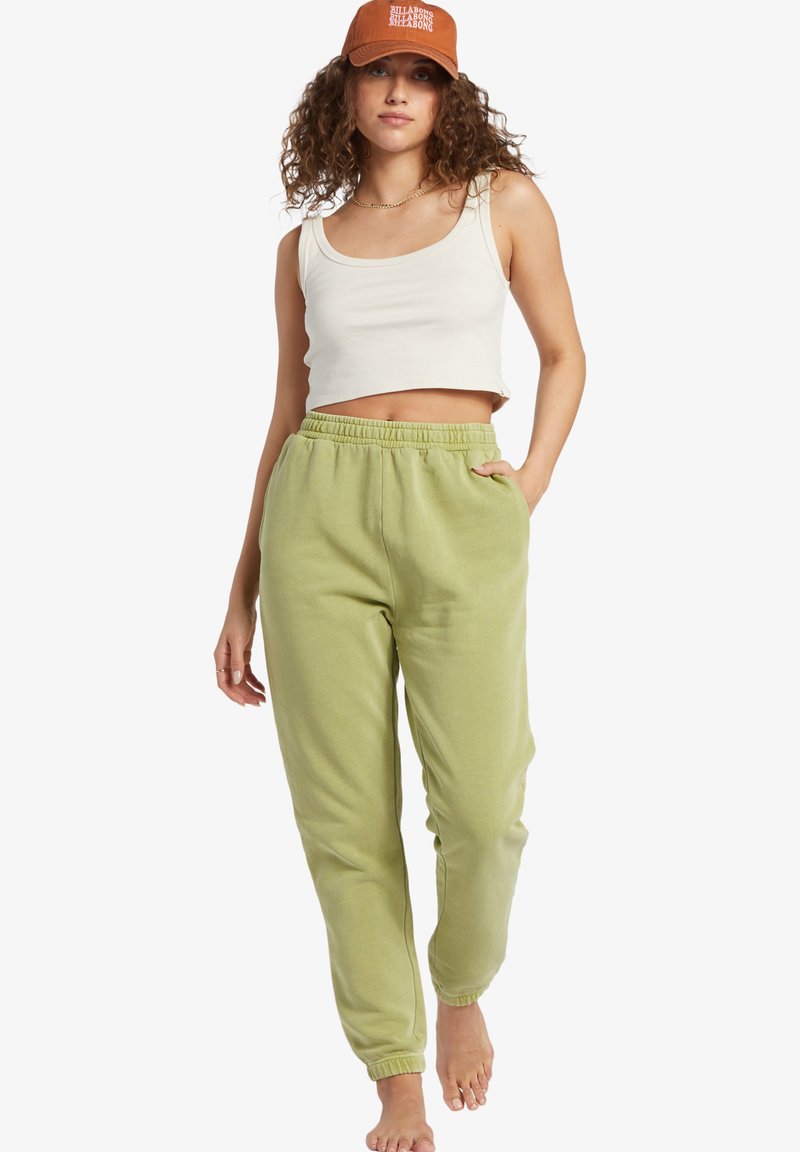 Lys grønne bomulds joggers med elastisk talje og sidelommer, parret med en hvid cropped tanktop og en brun kasket.