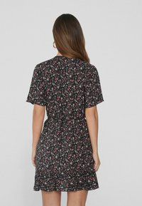 Schwarzes Blumenkleid mit kurzen Ärmeln, gerafftem Saum und tailliertem Schnitt. Es zeigt kleine pinke und grüne Blumen vor einem dunklen Hintergrund.