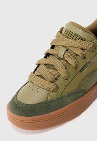 Olivengrøn Puma sneaker med tykke snørebånd, ruskind tåhætte, mærke på tungen og gummisål på hvid baggrund.