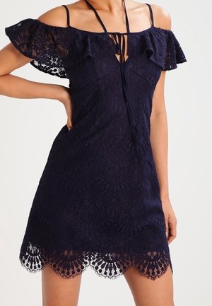 Marineblauwe off-shoulder jurk, met kantstof, gerimpelde mouwen, een strikkoord en een gegolfde zoom met ingewikkelde patronen.