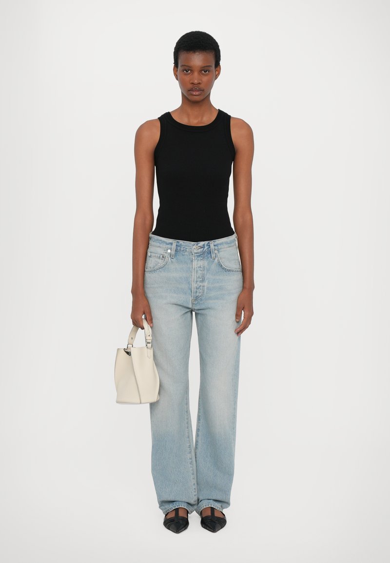 Top sans manches noir, jeans large bleu clair, sac à main blanc et ballerines noires pointues. Tissu lisse avec un style décontracté et des lignes épurées.