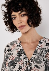 Button-up Hemd in hellbeige mit schwarzen Blumen- und abstrakten Mustern. Verfügt über eine lässige Passform, kurze Ärmel und einen kleinen Kragen.